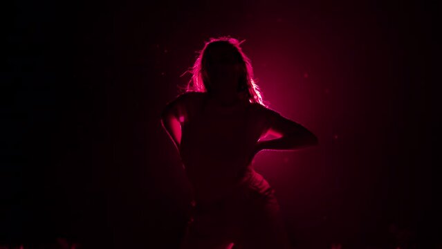 Young woman moves her head and hair in dark studio. Dancer performing dance on pink colorful spotlight background. Concept of sexual dancing with neon backlight.