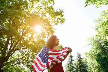 Young African american woman is waving American flag on top of at nature background. USA resident, US citizen. Immigration concept   
