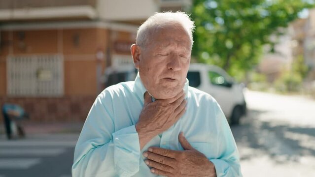 Senior grey-haired man coughing at street