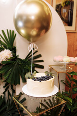 festive arch with white cake with berries, gold air balloon, white flowers, monstera leaves on birthday party. photo zone in restaurant.