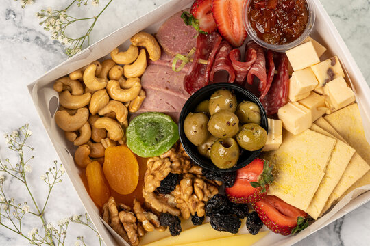 charcuterie box with cheeses, crackers, strawberries, olives, kiwi, grapes, pastrami, salami, apricot and walnuts