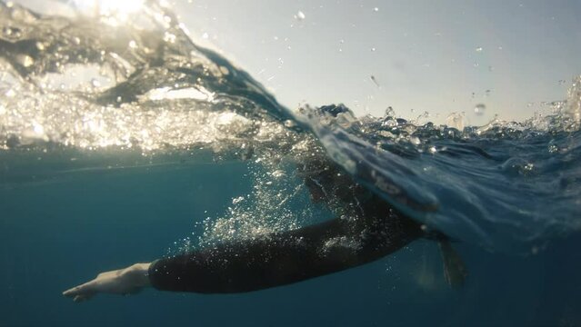 Sportswam swimming front crawl in sea at sunset, slow motion. Professional swimmer training in open water with sun shining in background, tracking shot