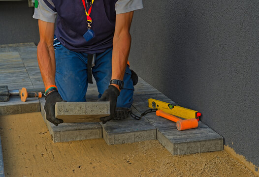 Handyman paver arranges paving stones. Construction of the pavement. Visible paving tools: laser level, rubber mallet, slide hammer and chisel.