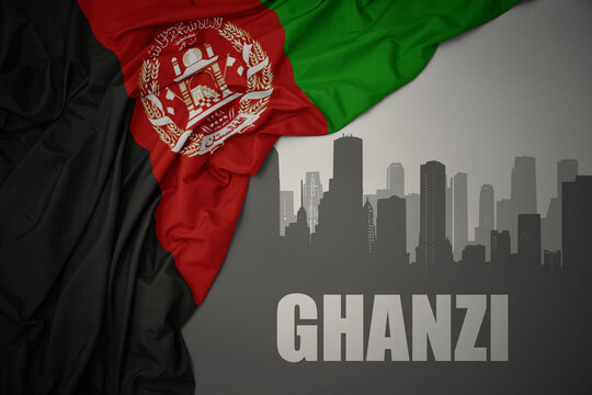 abstract silhouette of the city with text Ghazni near waving national flag of afghanistan on a gray background.