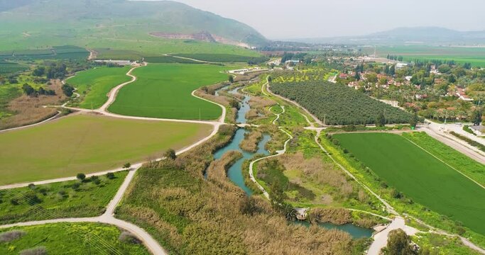 Aerial view of cultivated fields with hills in the background and Kibbutzim Stream, Nir David, Northern District, Israel.