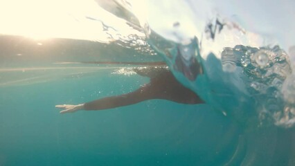 Male athlete swimming in open water, underwater view. Swimmer training in sea with sun shining through water, tracking shot. Sportsman wearing swimsuit exercising at sunset - Powered by Adobe