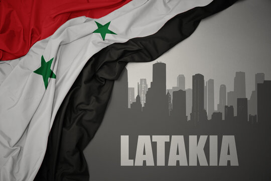 abstract silhouette of the city with text Latakia near waving national flag of syria on a gray background.
