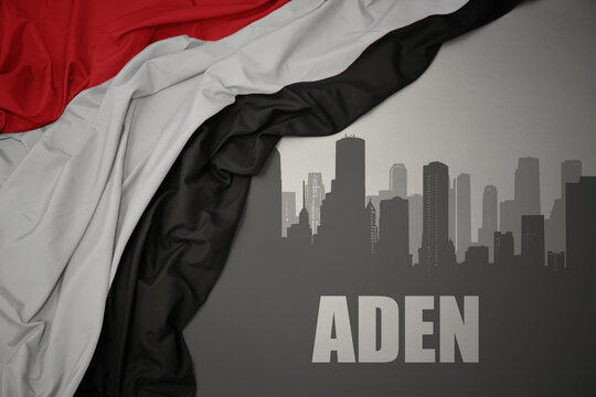 abstract silhouette of the city with text Aden near waving national flag of yemen on a gray background.