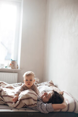 young mother and little daughter woke up in bed, having fun, hugging, looking at a book