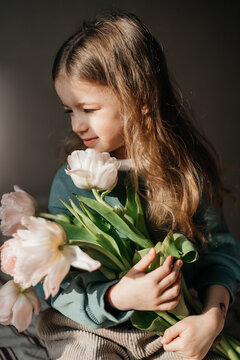 Portrait of a 4-year-old girl holding a bouquet of fresh pink tulips posing for a photo with morning light
