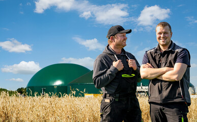 Energiewende - Biogas, stolzer Landwirt mit seinem Sohn vor einer Biogasanlage und Getreide.