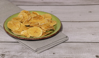 Fried plantain on green plate and white wooden table, overhead view