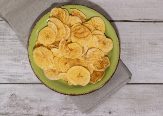 Fried plantain on green plate and white wooden table, overhead view