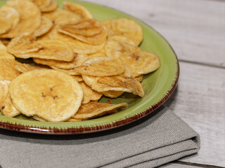 Fried plantain on green plate and white wooden table, close up view