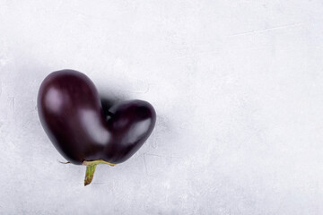 Heart shaped ugly eggplant isolated on concrete grey background, funny aubergine vegetables for a...