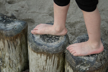 Obraz premium the child's feet carefully step on the small wooden breakwaters against the backdrop of the sea