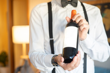 Fancy waiter showing a mockup red wine bottle in a trendy cozy bar