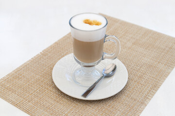 Latte in a transparent cup stands on a saucer with a spoon. Coffee on the table in the cafe.