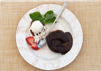 Chocolate fondant cake in the shape of a broken heart with ice cream, strawberries, mint on a white served table.