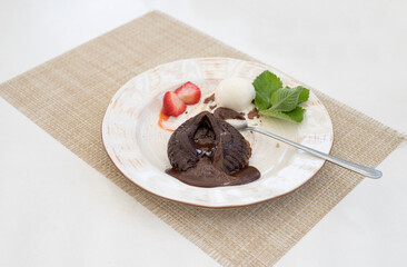Chocolate fondant cake in the shape of a broken heart with ice cream, strawberries, mint on a white served table.