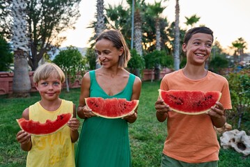 Sweet family, mother and her kids eating watermelon outdoor and having fun. High quality photo