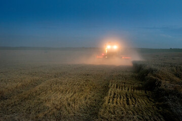 harvest at night, combine harvester in a wheat field, dust clouds illuminated by headlights