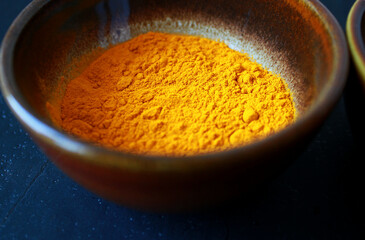 close-up of yellow turmeric spice powder in a brown ceramic bowl on dark background, isolated turmeric powder as exotic cooking spice