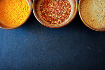 Three different dry spices in brown ceramic bowls on a dark background with space for text, turmeric and chili and ginger spice powder in bowls as cooking ingredients