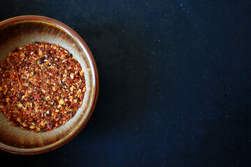 top view on red dry chili powder in a brown ceramic bowl on a dark background with space for text, directly above shot of chili powder as cooking ingredient