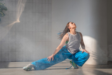 Youth jazz-funk dance style. Young and free, dancing in baggy clothes in a bright white hall. Stylish brunette in blue pants in a dynamic pose