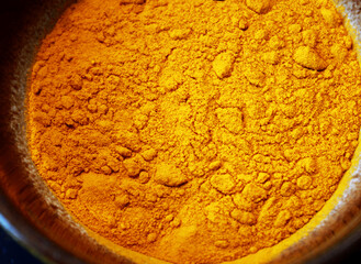 close up of dried yellow turmeric powder in a brown bowl, top view on yellow turmeric spice in a...