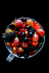 Berries of raspberries, mulberries, gooseberries and currants in a cup on a black background.