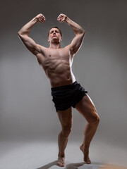 Fototapeta na wymiar Muscular man in an artistic pose, portrait on a gray background. The guy is an athlete in a wrestling pose. A muscular bodybuilder strains his fists