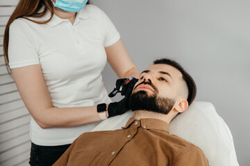 Obraz na płótnie Canvas Beauty treatments for a stylish young man with a beard. Beautician makes beauty injections in a man's face