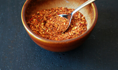 close-up of red dry chili powder in a brown ceramic bowl with a spoon on a dark background with space for text, red chili powder as cooking ingredient
