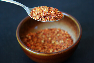 Red chili spice powder in a brown bowl on dark background, chili cooking spice powder on a spoon