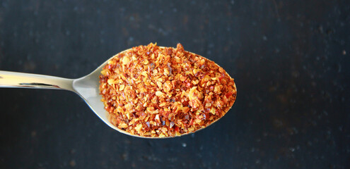 close-up of red hot chili spice powder on a spoon on black dark background with space for text