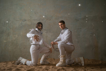 Astronauts on a deserted planet, a man and a woman in white spacesuits with large glass helmets sit...
