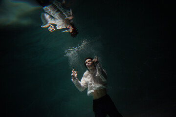 underwater shooting with contrasting light, a guy in a white shirt and pants screaming underwater, panicking and afraid of drowning, falling into the water, a crime.