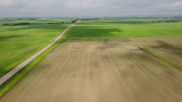 Aerial flight over prairie farm fields and a rural highway as moving cloud shadows travel across the landscape in Alberta Canada.