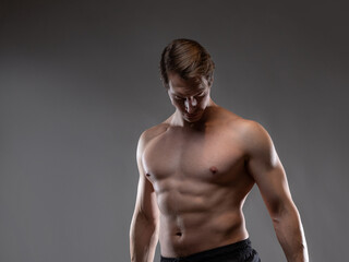 A muscular man expressively emotionally poses on a gray background. The guy is an athlete with pumped-up muscles. beautiful body relief.