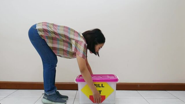 Asian woman lifting the box with one eye closed postoperatively. One of the activities that are not recommended after eye surgery or cataract surgery
