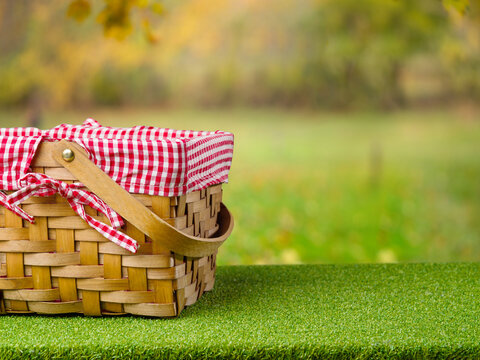 A straw picnic basket on a green lawn against the backdrop of a beautiful autumn nature. Family outdoor recreation, romance, vacation with friends. There is free space to insert.