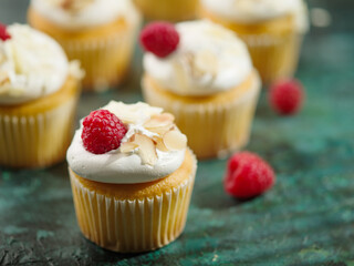 Lots of appetizing berry muffins with light airy cream, raspberries, almonds on a dark green background. Banquet, picnic, birthday. Advertising, banner, holiday invitation.