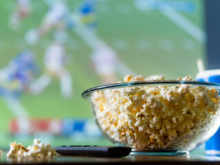 A sports program on the TV screen, a large bowl of popcorn and a TV remote control. Close-up. Rest in front of TV sports fan, fast food. Advertising, banner, poster.