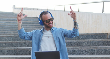 Young Caucasian boy sitting on stairs singing happily with headphones on and arms up. 