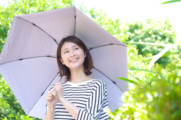 日差しの強い公園で日傘をさして紫外線対策をする笑顔の若い女性