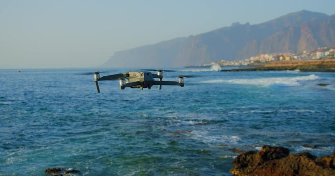 Remote controlled unrecognizible drone flies over water. High resolution video camera flying above the sea against a sunset sky.