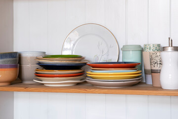 Wooden shelf with kitchen utensils, rustic style. Tableware, plates and bowls stand on a shelf in the kitchen. Cupboard with set of colourful dishes, modern interior.