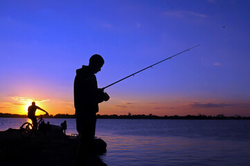 Silhouette of man fishing in Guaiba lake next to Gasometro at sunset time, in Porto Alegre, Rio Grande do Sul, Brazil